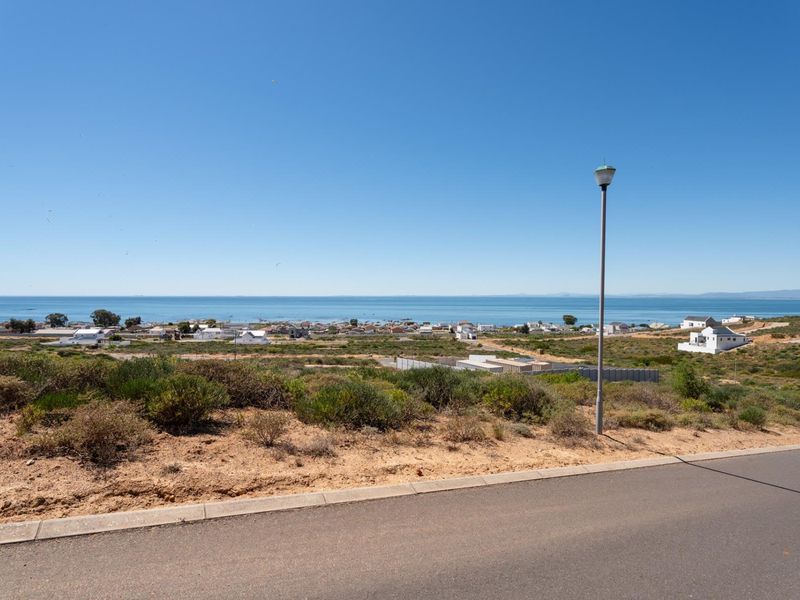 A scenic view of the coastline and surrounding residential area from a paved street, highlighting the elevated position of the vacant land.