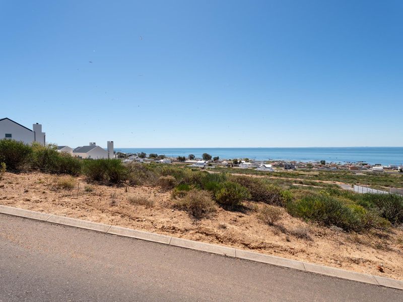 A clear view of the coastal landscape and ocean from the elevated vacant residential plot, featuring paved road access and established curbing.