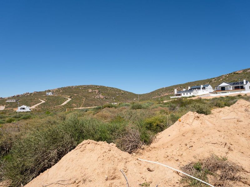 A wide-angle view of the vacant residential land featuring natural fynbos vegetation, sloped topography, and surrounding hillside residential developments.