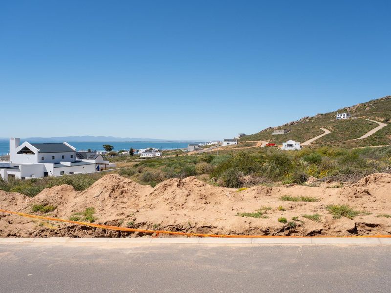 A scenic view of a coastal residential area featuring a paved road in the foreground and surrounding hillside landscape.