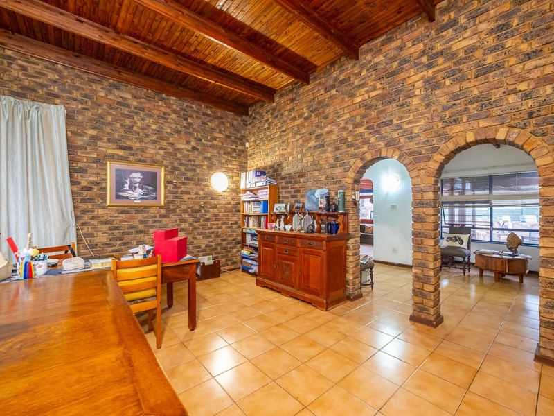 Spacious living area featuring rustic exposed brick walls, a high timber raked ceiling, and classic ceramic floor tiles with distinctive brick archway transitions.
