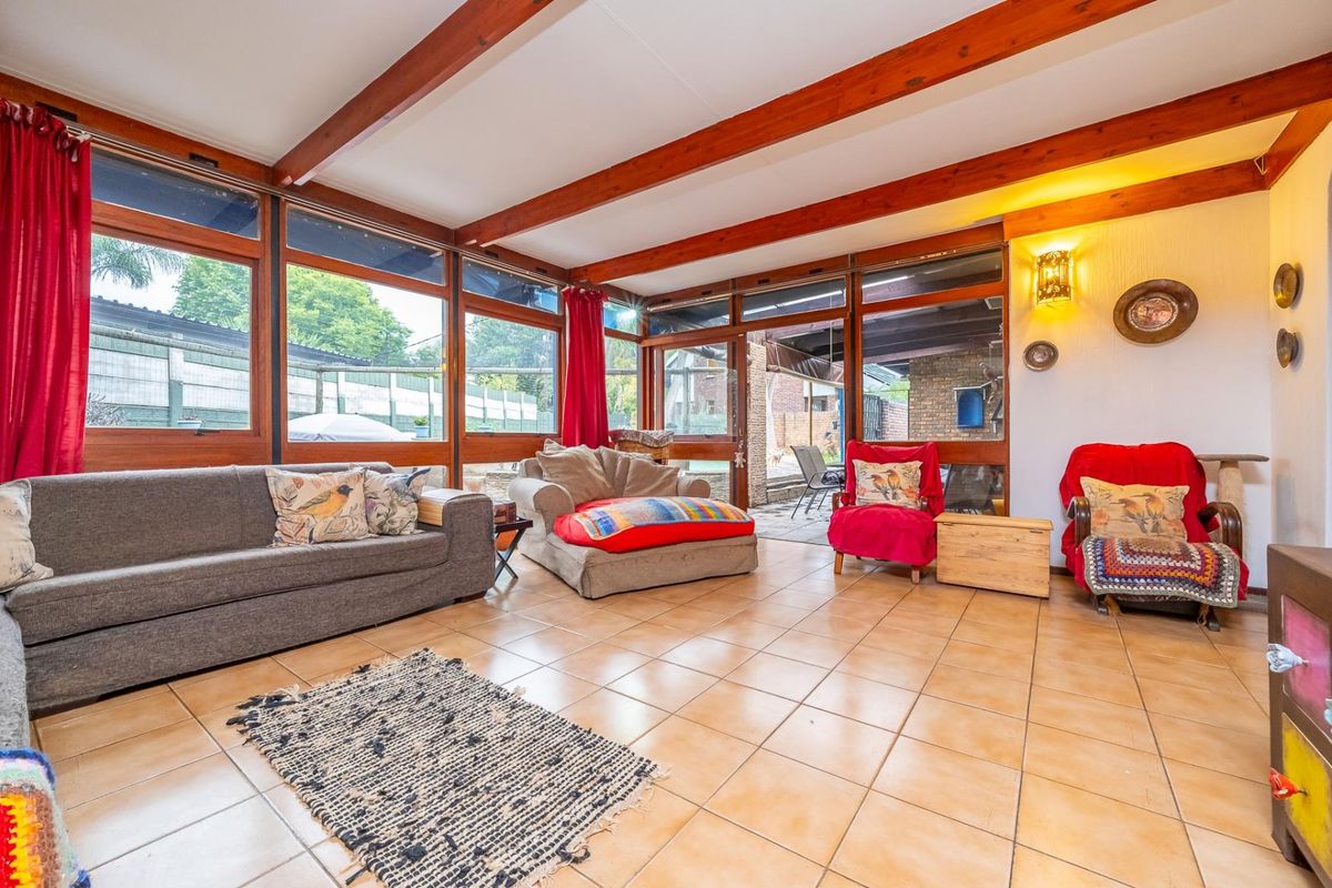 Spacious living room featuring exposed timber ceiling beams, large windows providing ample natural light, and ceramic tiled flooring with direct access to the patio.