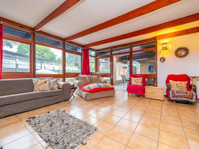 Spacious living room featuring exposed timber ceiling beams, large windows providing ample natural light, and ceramic tiled flooring with direct access to the patio.