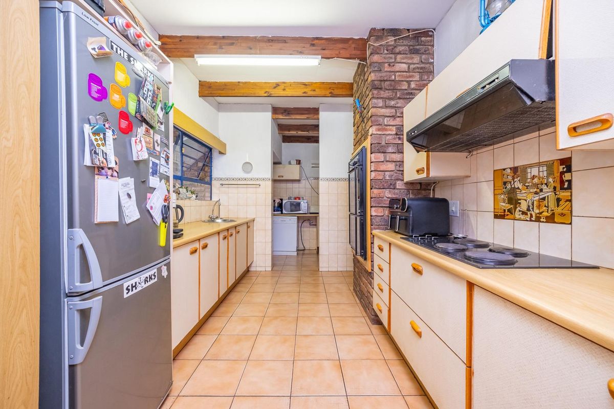 A functional kitchen featuring exposed timber ceiling beams, a brick feature wall, built-in cabinetry, and integrated cooking appliances with tiled flooring throughout.