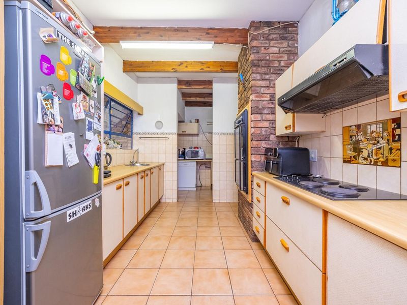 A functional kitchen featuring exposed timber ceiling beams, a brick feature wall, built-in cabinetry, and integrated cooking appliances with tiled flooring throughout.