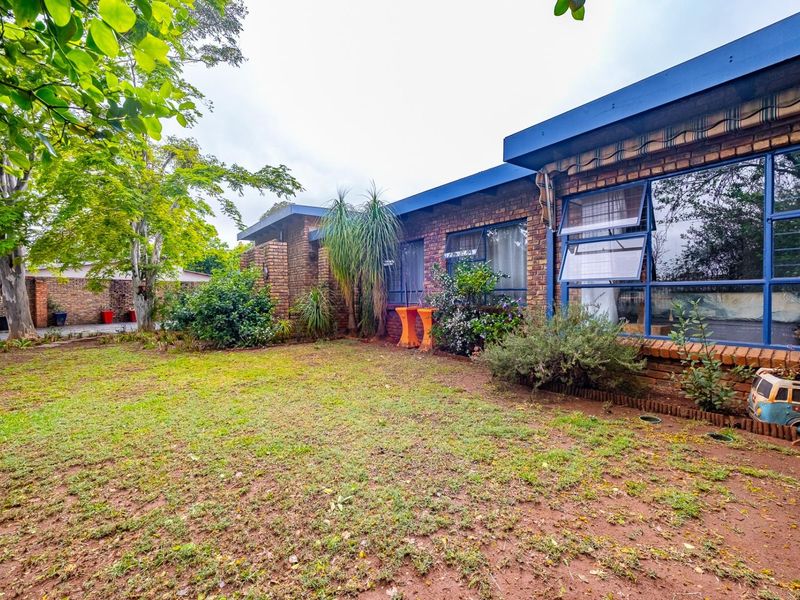 A rear view of the house featuring a face brick facade, large steel-framed windows with security bars, and a spacious garden area.