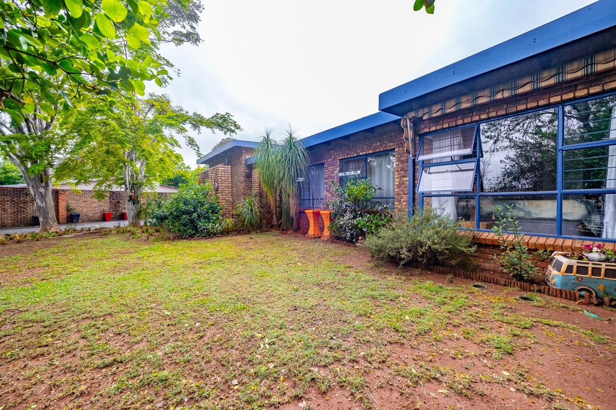 A rear view of the house featuring a face brick facade, large steel-framed windows with security bars, and a spacious garden area.