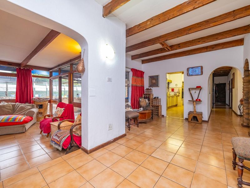 Open plan living area featuring exposed timber ceiling beams, ceramic floor tiles, and arched architectural details connecting to the kitchen and hallway.