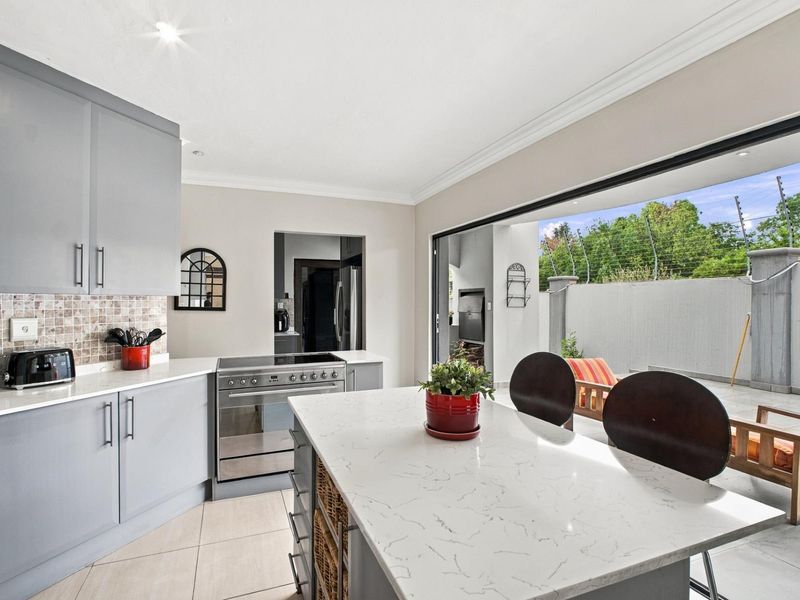 Modern kitchen featuring a central island with stone countertops, grey cabinetry, and seamless flow to an outdoor patio area through large sliding glass doors.