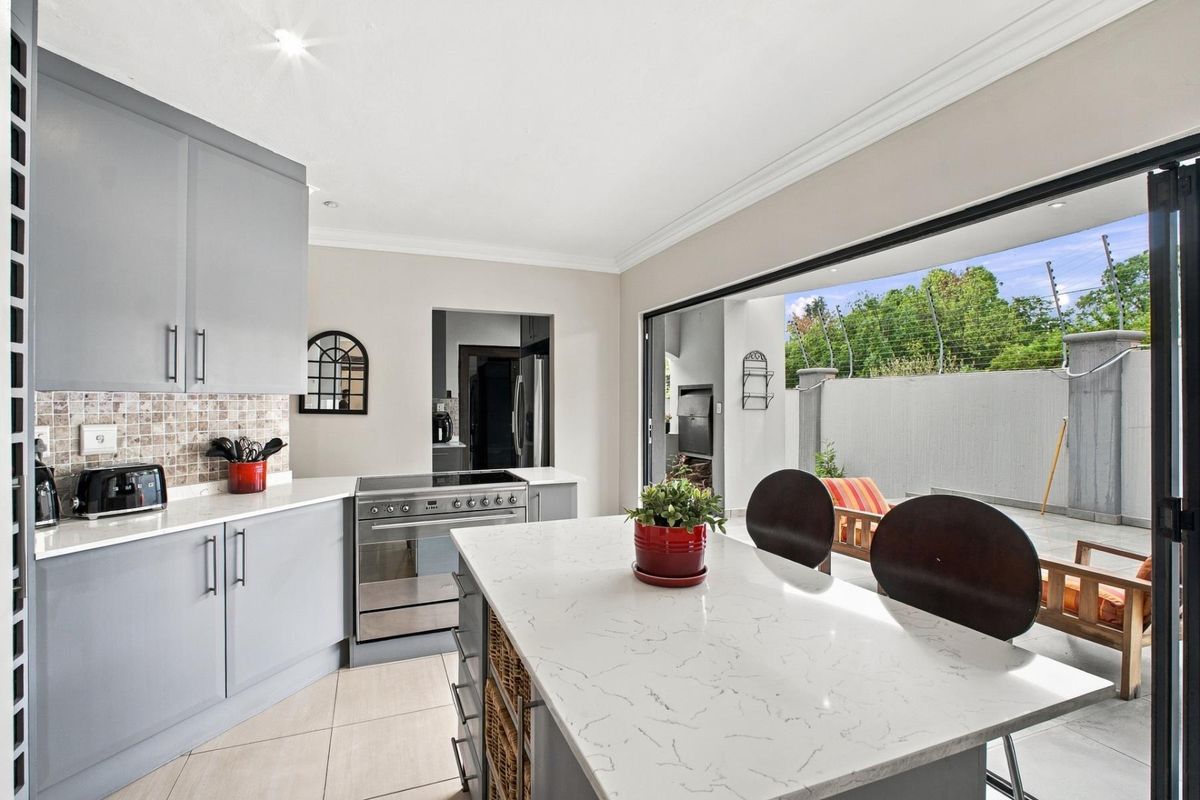 Modern kitchen featuring a central island with stone countertops, grey cabinetry, and seamless flow to an outdoor patio area through large sliding glass doors.