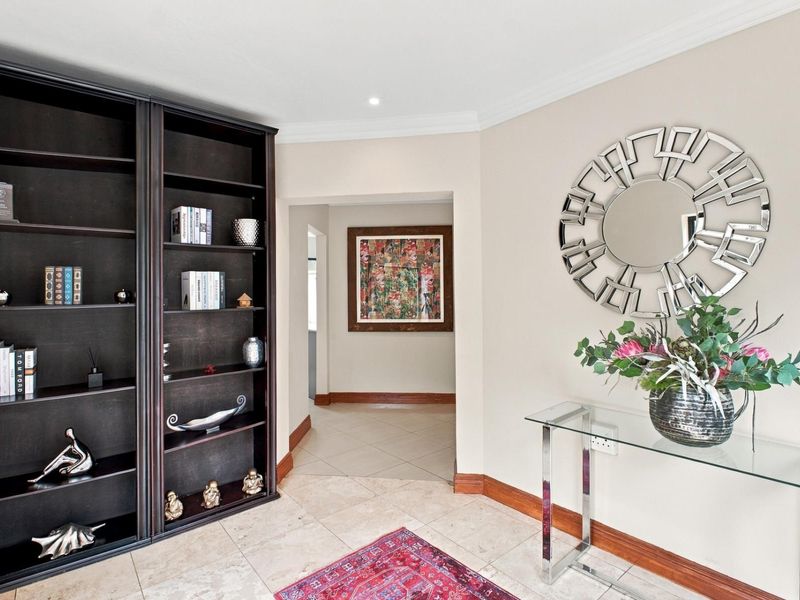 A well-maintained entrance hallway featuring tiled flooring, coving, and a large built-in shelving unit, leading into the interior of the home.