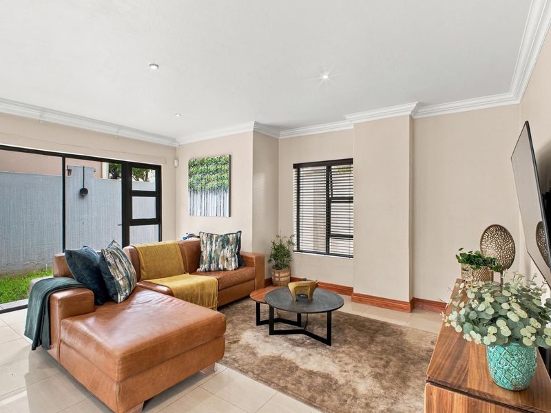 A bright and well-maintained living room featuring tiled flooring, modern cornicing, and large sliding glass doors that provide access to the outdoor area.