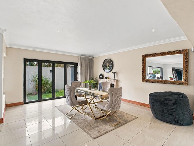 Spacious dining area featuring polished tiled flooring, decorative cornicing, and black aluminium folding doors providing seamless access to the outdoor garden space.