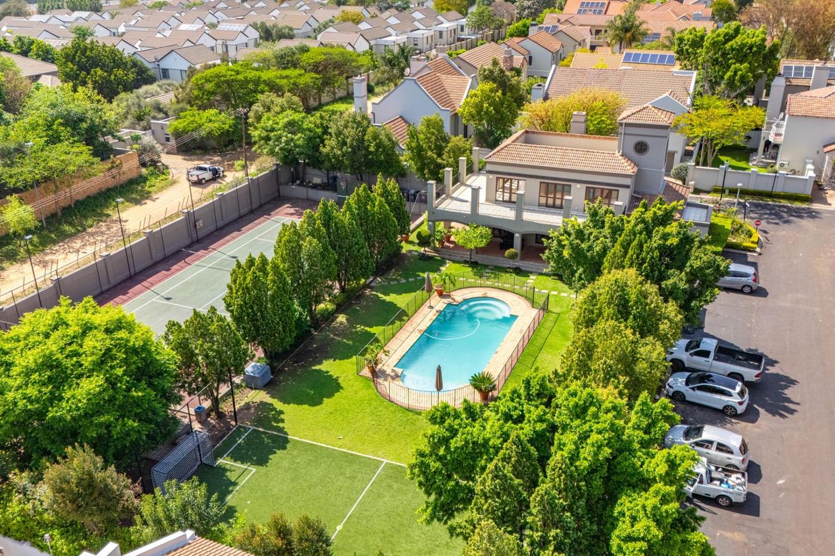 Aerial view of a residential property featuring a swimming pool, private tennis court, landscaped garden, and spacious patio area.