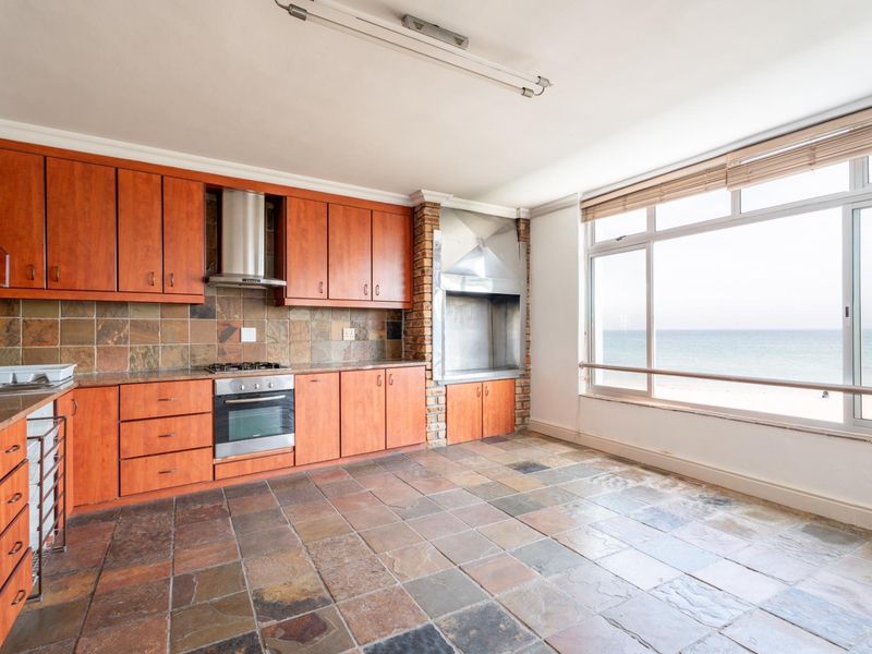 Open-plan kitchen featuring built-in cabinetry, stone flooring, and an indoor braai, with large windows offering direct ocean views.