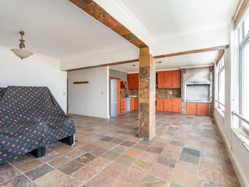 Open-plan living and kitchen area featuring slate tile flooring, built-in wooden cabinetry, and a built-in indoor braai with a stainless steel extractor.
