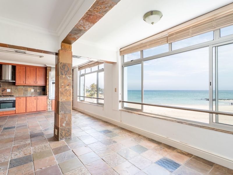 Open-plan kitchen and living area featuring stone tile flooring, built-in cabinetry, and expansive windows offering direct ocean views.