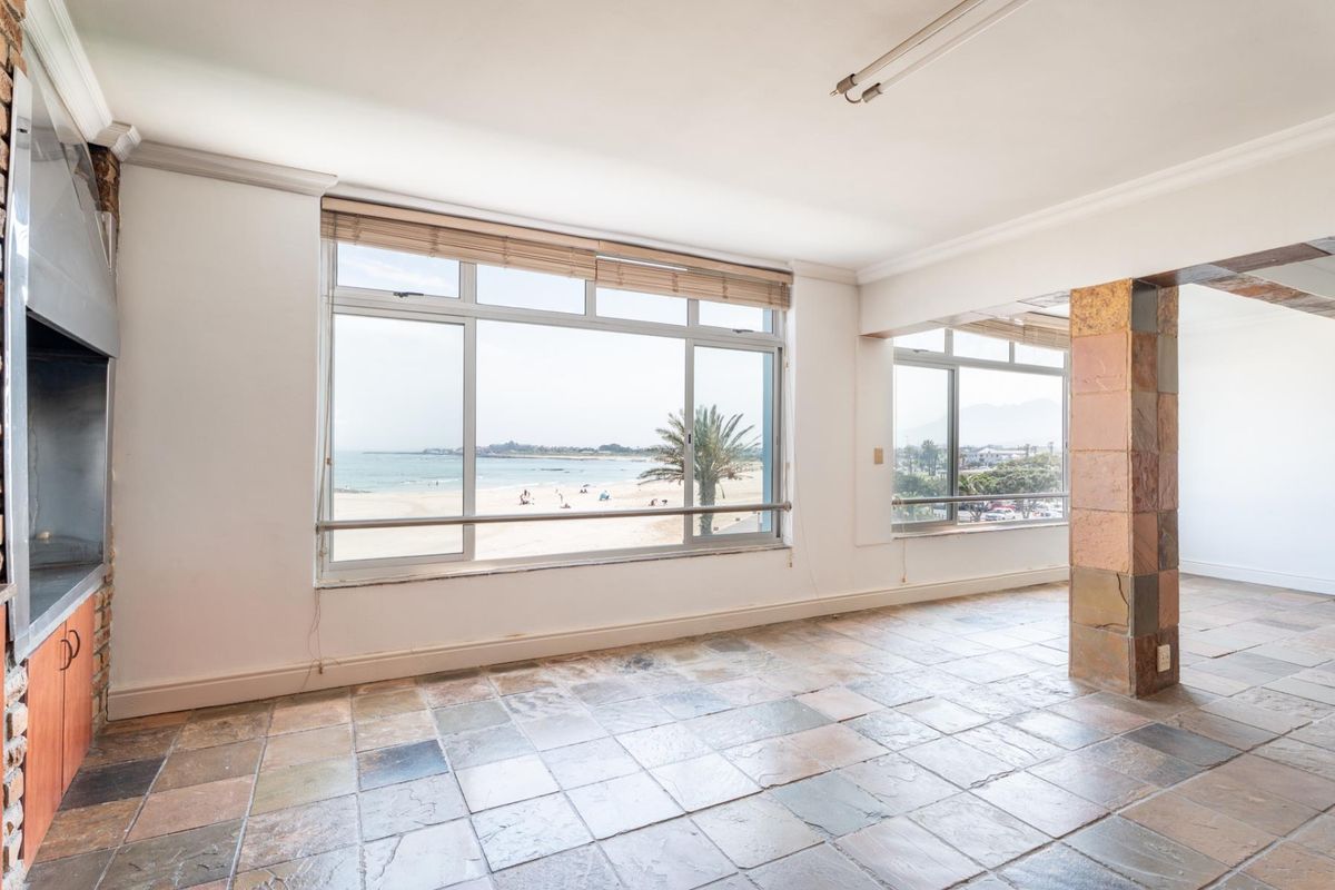 Spacious living area featuring stone tile flooring, a built-in fireplace, and large windows offering panoramic beach and ocean views.