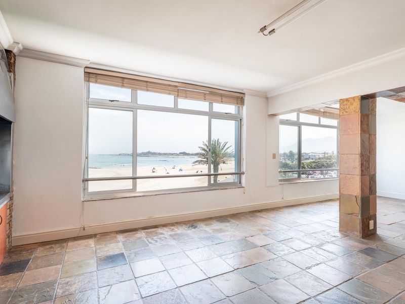Spacious living area featuring stone tile flooring, a built-in fireplace, and large windows offering panoramic beach and ocean views.