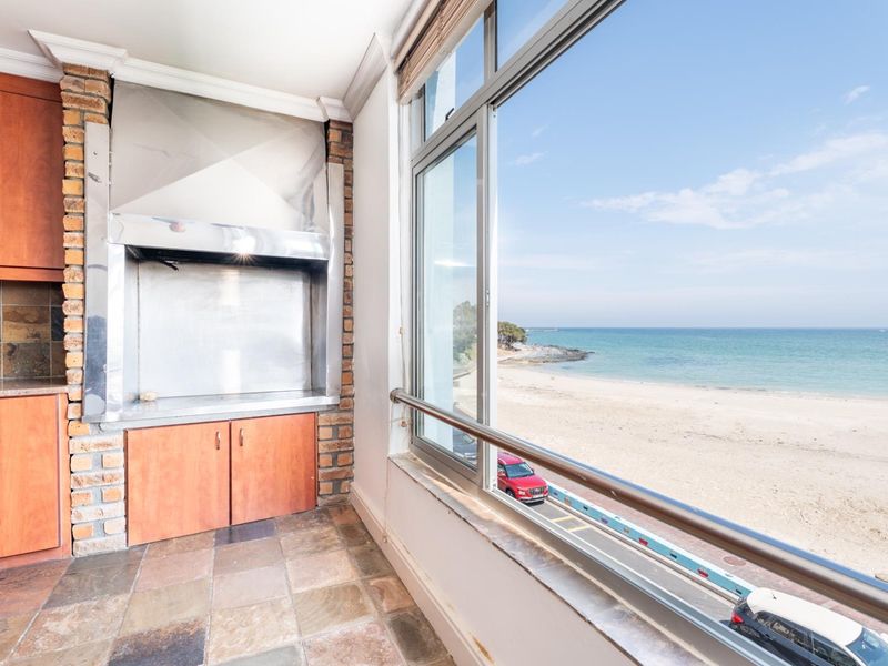 Enclosed balcony featuring a built-in braai with stainless steel extractor, stone tile flooring, and expansive ocean views.