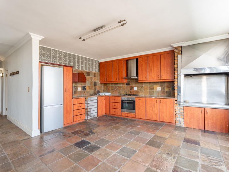 Spacious kitchen featuring wooden cabinetry, built-in oven and hob, integrated braai area, and durable stone tile flooring throughout.