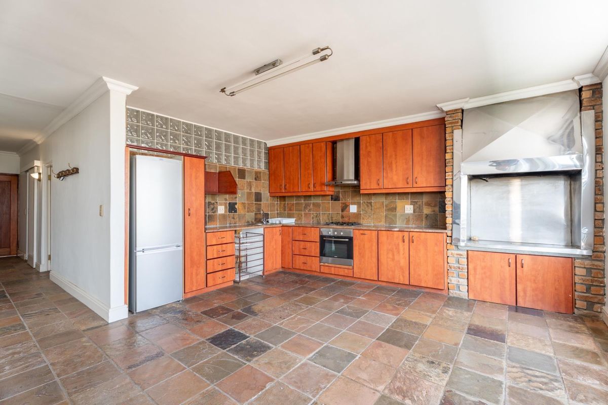 Spacious kitchen featuring wooden cabinetry, built-in oven and hob, integrated braai area, and durable stone tile flooring throughout.