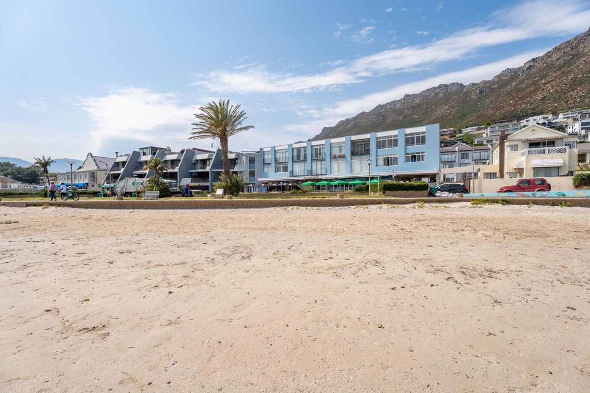 A wide-angle view of the apartment building complex situated directly along the beachfront, showcasing its proximity to the coast and surrounding mountain landscape.