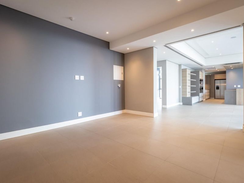 Spacious open-plan living and kitchen area featuring neutral tiled flooring, modern recessed lighting, and sleek built-in cabinetry with integrated appliances.