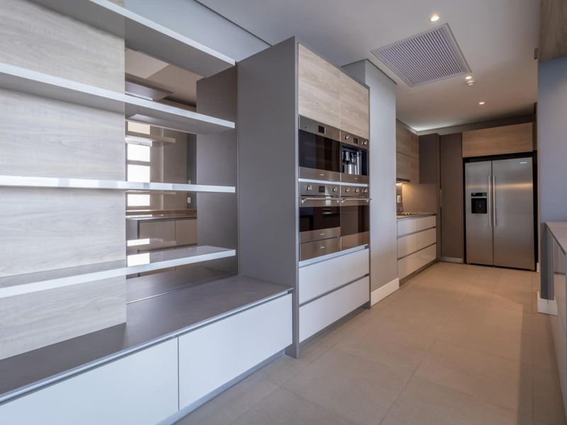 Modern kitchen featuring sleek built-in cabinetry, integrated appliances, floating shelving, and neutral tiled flooring in a clean, contemporary design.