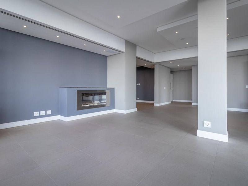 Spacious, modern open-plan living area featuring neutral grey tones, tiled flooring, recessed ceiling lighting, and a sleek built-in fireplace.