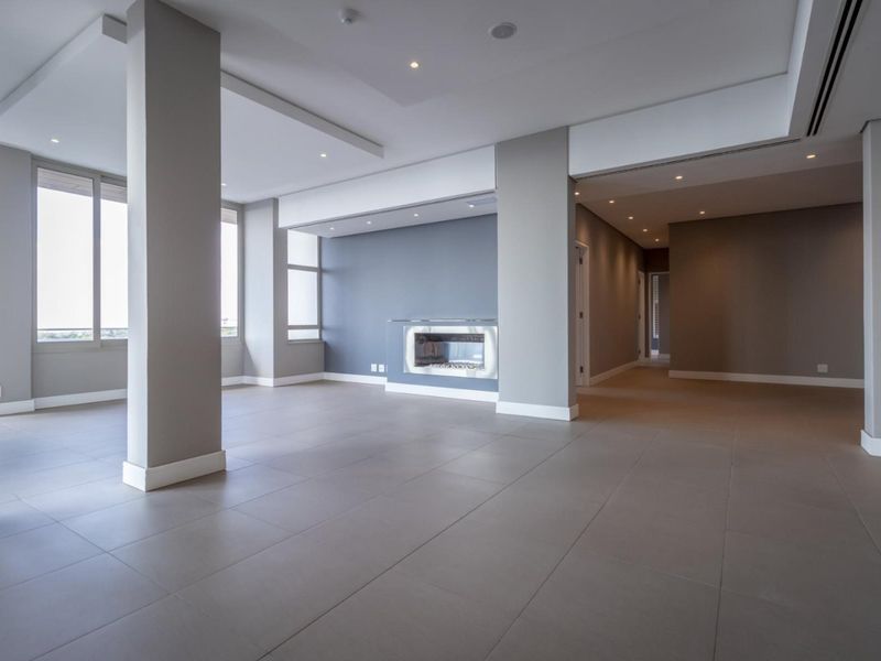 Spacious, modern open-plan living area featuring neutral tiled floors, recessed ceiling lighting, structural columns, and a sleek built-in fireplace.
