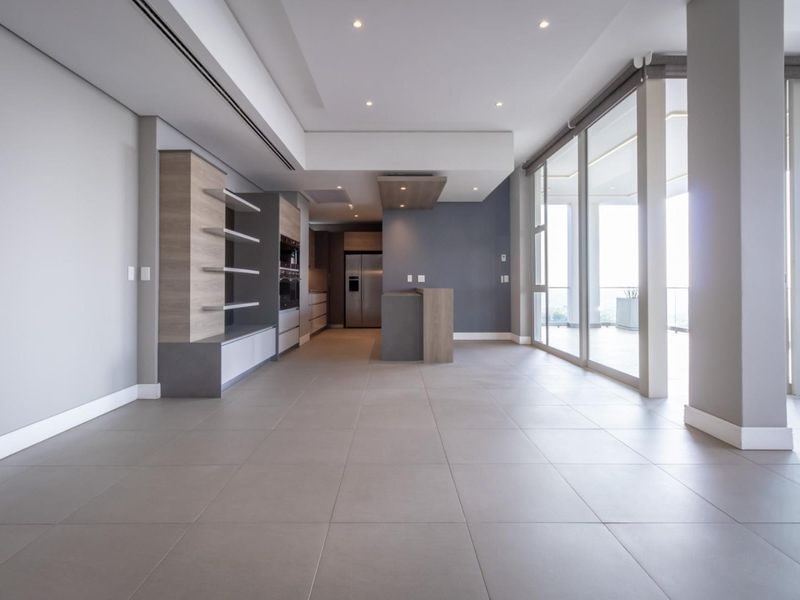 Spacious open-plan living and kitchen area featuring modern built-in cabinetry, integrated appliances, large format floor tiles, and expansive sliding doors leading to a balcony.