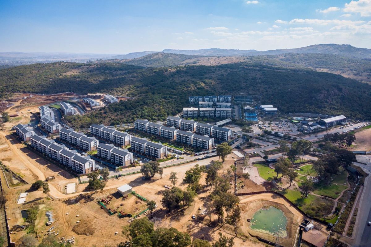 Aerial view of a modern residential apartment complex development set within a scenic landscape with surrounding hills and established greenery.