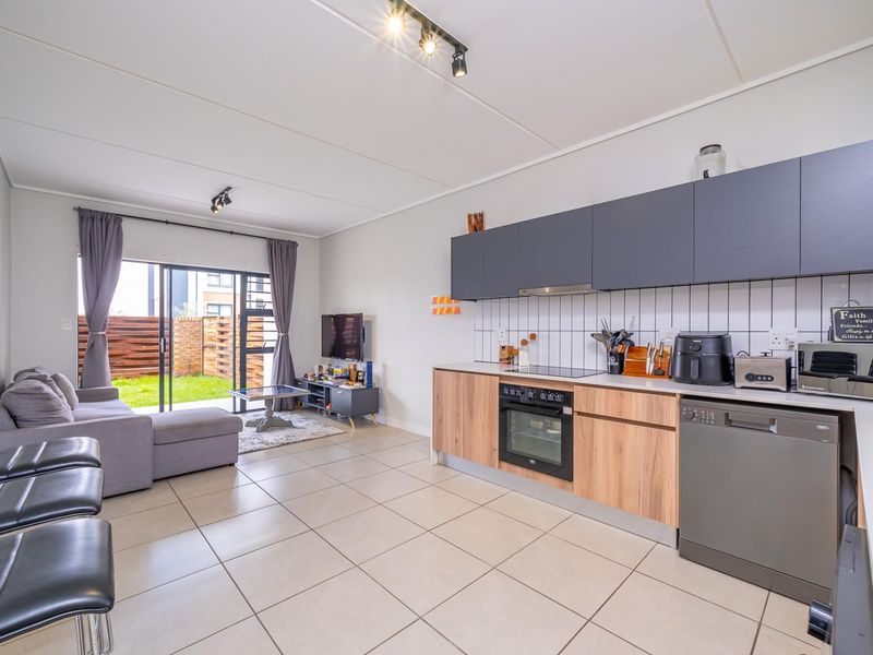 Modern open-plan living area featuring a contemporary kitchen with wood-finish cabinetry, tiled floors, and direct access to a private garden through sliding doors.