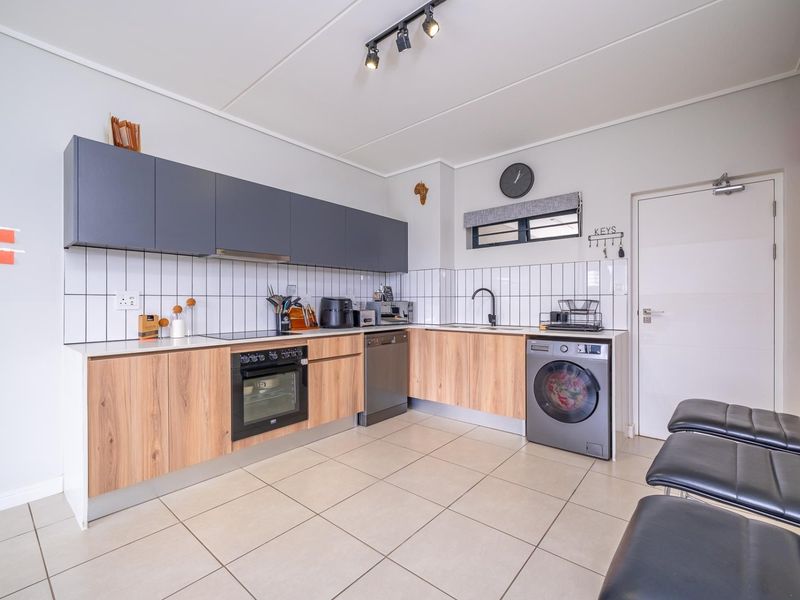 Modern kitchen featuring wood-grain lower cabinetry, dark grey upper cabinets, tiled backsplash, built-in oven, hob, and integrated dishwasher with tiled flooring.