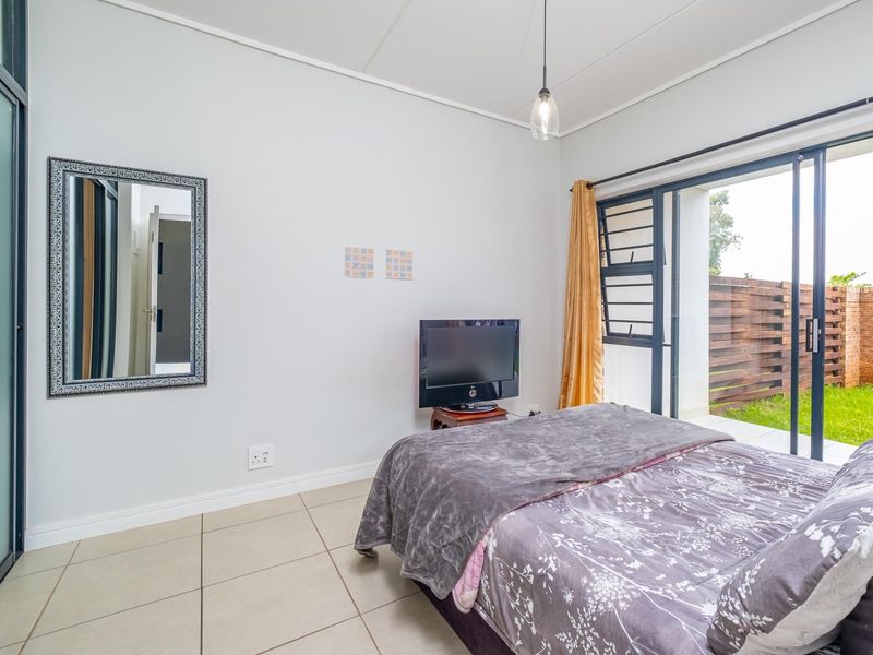 A bright bedroom featuring tiled flooring, a pendant light, and large sliding glass doors providing direct access to an outdoor patio area.