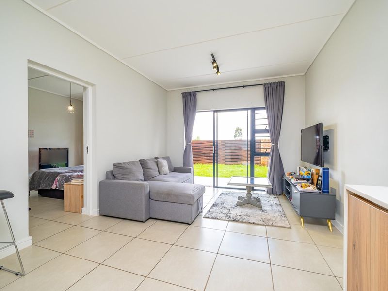 A bright, open-plan living area featuring neutral tiled flooring, modern track lighting, and a sliding glass door providing direct access to the rear garden.