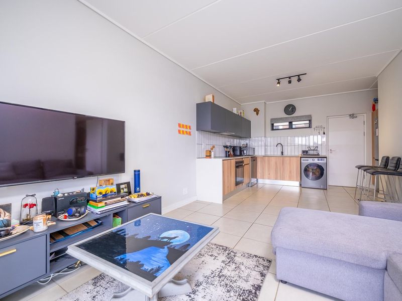 Open-plan living area featuring a modern kitchen with wood-finish cabinetry, tiled flooring, and integrated appliances, seamlessly flowing into the lounge space.
