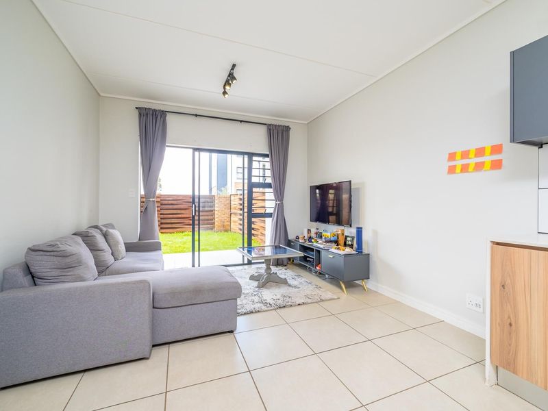 An open-plan living area featuring tiled flooring, modern track lighting, and a sliding glass door providing direct access to the rear garden.
