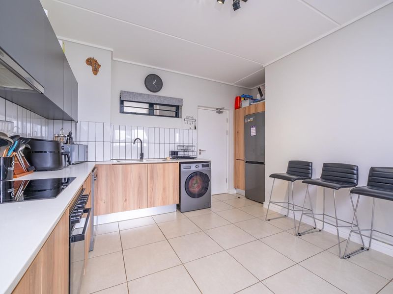 Modern kitchen featuring wood-tone cabinetry, white subway tile backsplash, integrated appliances, and tiled flooring with a breakfast bar area.