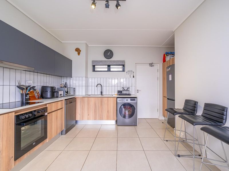 Modern kitchen featuring wood-finish cabinetry, dark grey upper cupboards, tiled backsplash, built-in oven, hob, and integrated laundry appliance space.