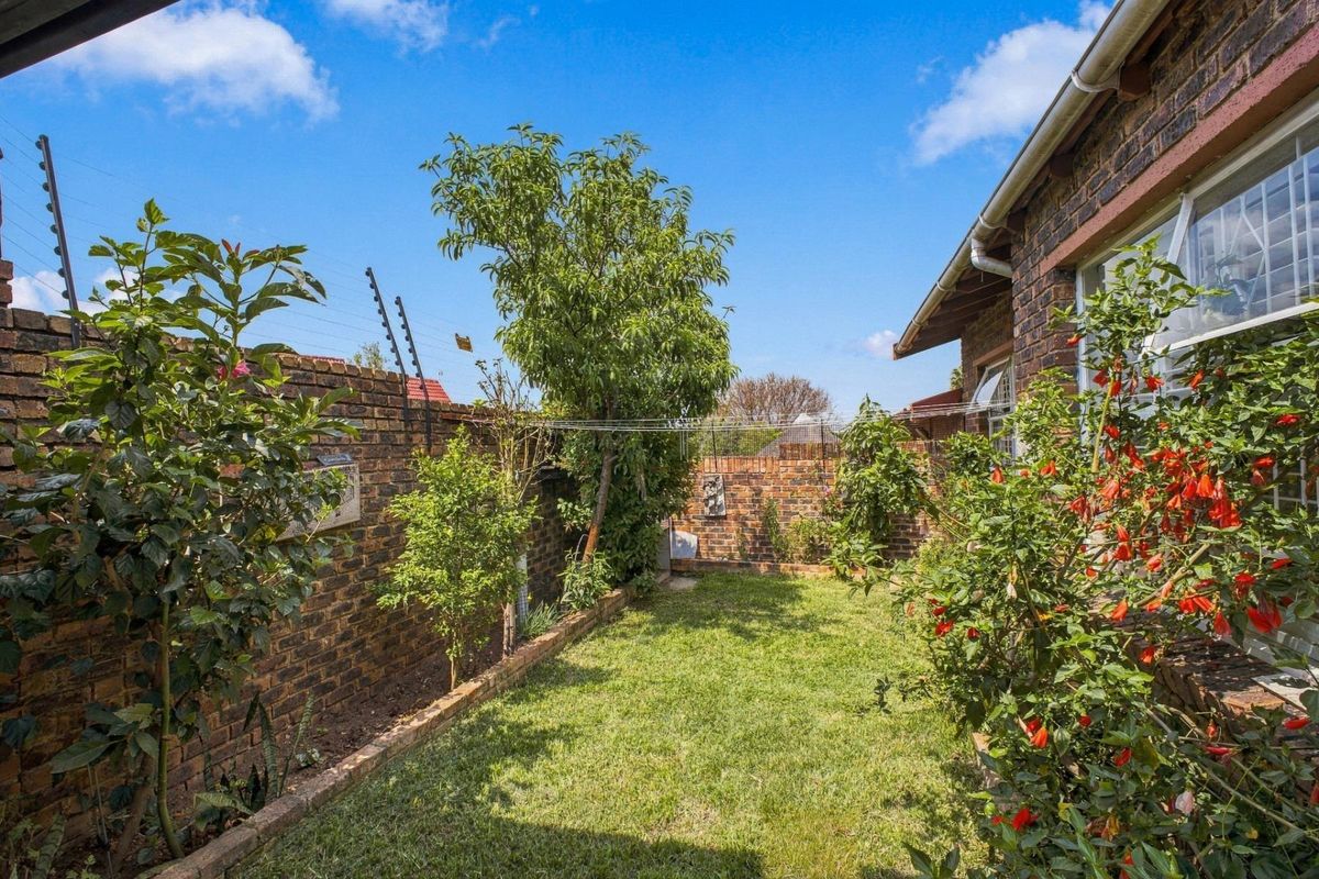 A private rear garden featuring a well-maintained lawn, established perimeter brick walls with electric fencing, and mature garden beds.