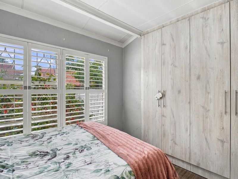 A well-maintained bedroom featuring light wood-grain built-in cupboards and white plantation shutters, providing a clean and functional living space.