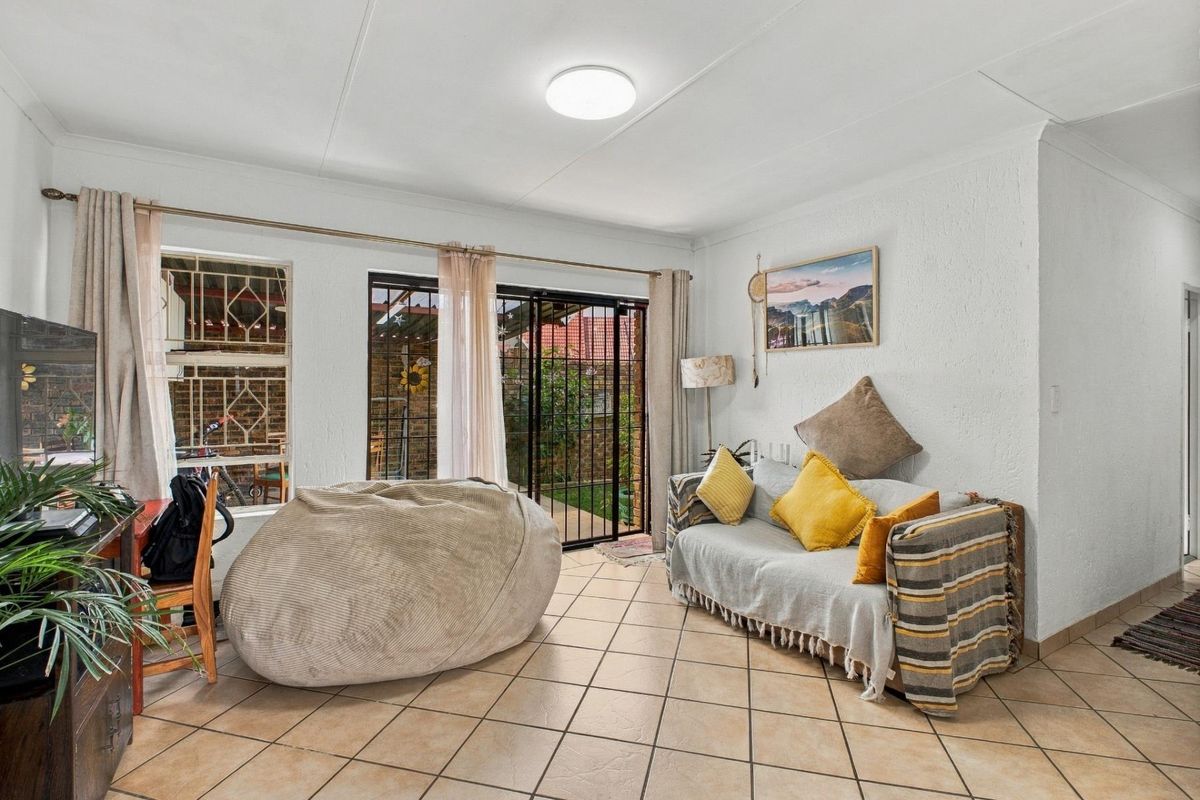 A living room featuring ceramic floor tiles, a sliding glass door with security gate, and direct access to the outdoor area.