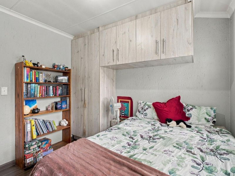A well-maintained bedroom featuring light wood-grain built-in cabinetry with overhead storage and functional window blinds.