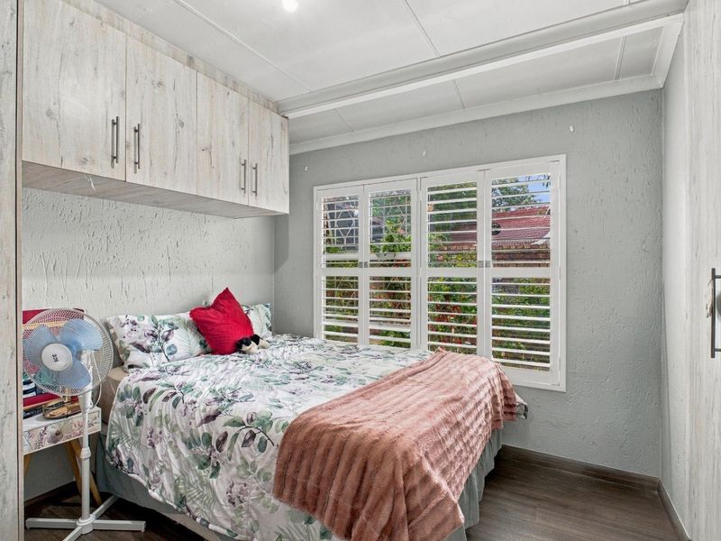 A well-maintained bedroom featuring built-in cupboards, overhead storage units, and white plantation shutters that provide natural light and privacy.