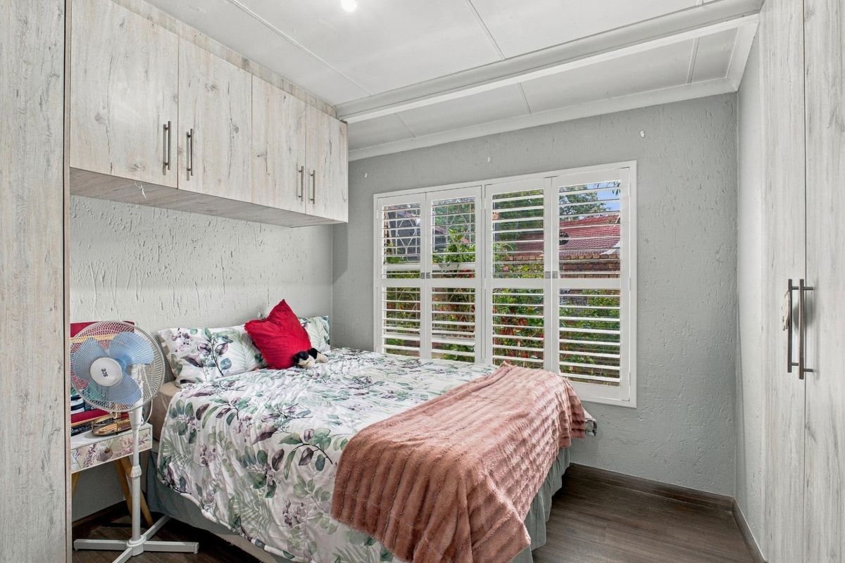 A well-maintained bedroom featuring built-in cupboards, overhead storage units, and white plantation shutters that provide natural light and privacy.