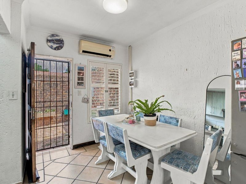 A dining area featuring tiled floors, a wall-mounted air conditioning unit, and a security gate leading to the exterior.
