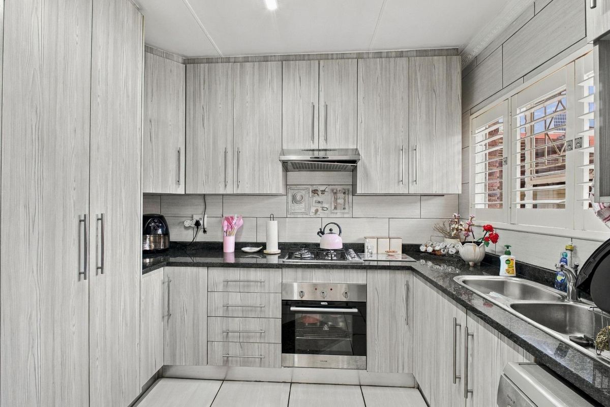 Modern kitchen featuring light wood-grain cabinetry, granite countertops, stainless steel oven, gas hob, extractor fan, and double basin sink with plantation shutters.
