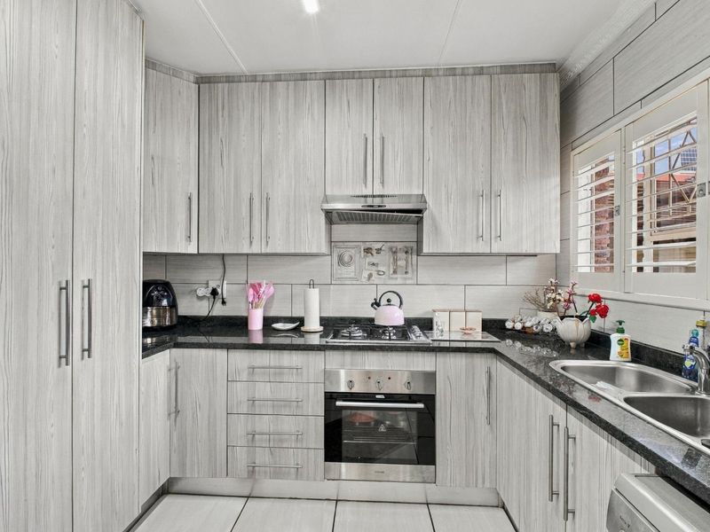 Modern kitchen featuring light wood-grain cabinetry, granite countertops, stainless steel oven, gas hob, extractor fan, and double basin sink with plantation shutters.